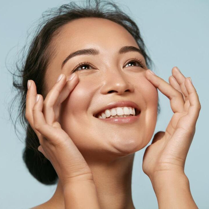 woman smiling with bright eyes looking up to the skin while touching both of her cheeks with each hand at the highest point of her cheekbones